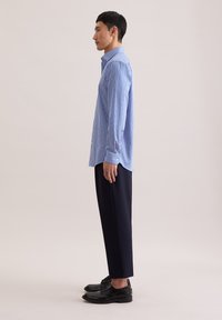 Pasiasta niebieska koszula na guziki wykonana z lekkiej tkaniny, w połączeniu z czarnymi, dopasowanymi spodniami i czarnymi sznurowanymi butami.