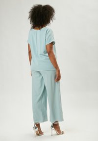 Completo a due pezzi di un blu chiaro, composto da una maglietta a maniche corte e pantaloni a gamba larga, realizzato in tessuto morbido, con sandali alti con tacco in argento lucido.