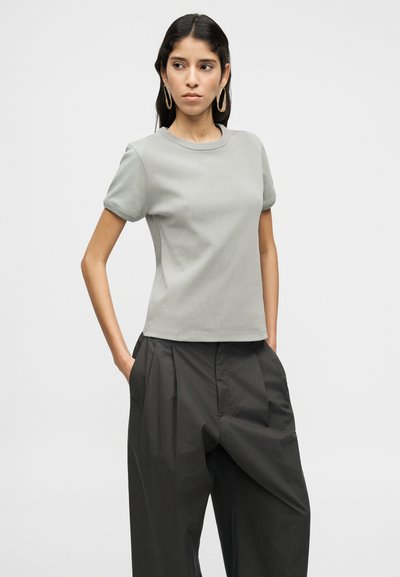 Ανοιχτό γκρι εφαρμοστή μπλούζα με κοντά μανίκια και στρογγυλή λαιμόκοψη, με απαλό υφή, συνδυασμένη με ψηλόμεσο σκούρο παντελόνι με πιέτες μπροστά.