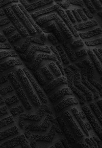 Čierna textúrovaná látka s vyvýšenými geometrickými vzormi. Dizajn obsahuje čiary a cikcaky, čím vytvára hmatateľný povrch. Mäkký materiál.