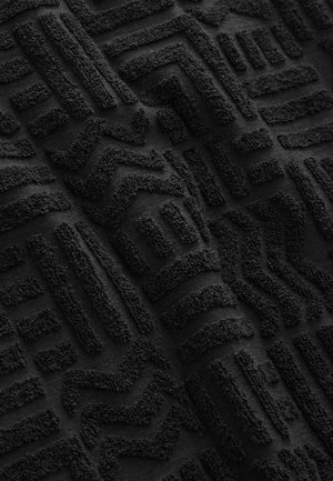 Schwarz strukturiertes Gewebe mit erhabenen geometrischen Mustern. Das Design umfasst Linien und Zickzackmuster, die eine taktile Oberfläche schaffen. Weiches Material.