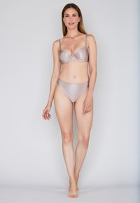 Woman standing barefoot wearing matching beige striped bra and high-cut panties against a plain light gray background.