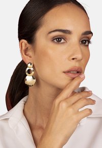 Orecchini dorati con tre pezzi connessi: una parte superiore circolare, una sezione mediana ovale e una base a disco martellato, che riflettono la luce sotto angolazioni diverse.