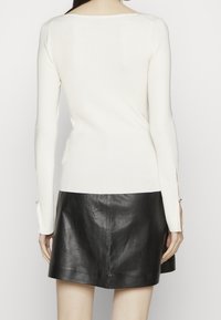 Top lungo a maniche con coste bianche, scollo a barca e fessure laterali, abbinato a una minigonna in pelle nera. Texture liscia, design aderente.