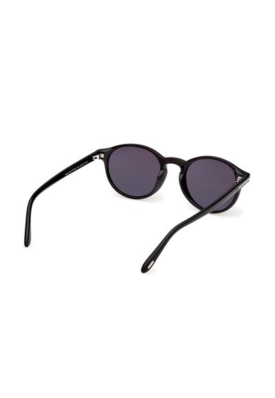 Lunettes de soleil noires à monture ronde avec verres foncés, branches légèrement écartées, présentées sur un fond blanc.
