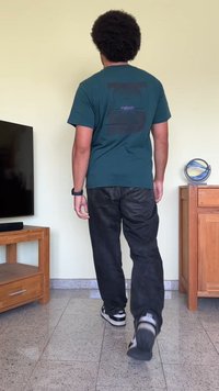 Camiseta de algodão verde escuro com um gráfico preto e texto roxo nas costas, combinada com calças de ganga pretas e ténis pretos.