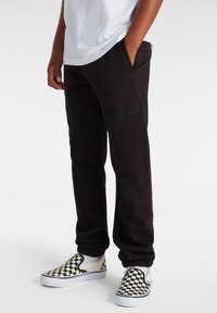 Zwarte sweatpants met zijzakken en elastische boorden, met een zwart Vans logo patch. Gecombineerd met zwart-wit geblokte instappers.