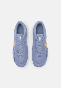 Las zapatillas de malla azules cuentan con un acento amarillo en el lateral, puntera redonda y cuello acolchado. Tienen un diseño con cordones y una suela blanca.