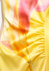 Κίτρινο σατέν ύφασμα με μεγάλα ροζ και πορτοκαλί λουλούδια και ρίγες με πιέτες στο πλάι του ενδύματος.