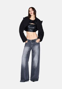 Zwarte cropped jas met gestructureerde schouders, gecombineerd met een aansluitende zwarte leren top met een uitsnijding. Wijde, vervaagde grijze spijkerbroek.