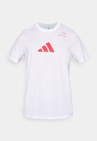 Valge puuvillane T-särk, millel on punane Adidas logo kolmnurga kujunduses ja tekst vasakus ülanurgas. Lühikesed varrukad, ümara kaelusega.