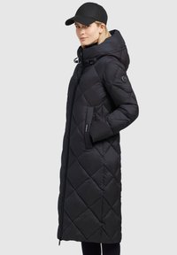Black quilted puffer coat with a hood, featuring a diagonal pattern, side pockets, and a zipper, paired with a black cap.
