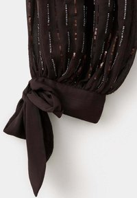 Manche en tissu transparent marron foncé avec des sequins verticaux et un détail de poignet noué.