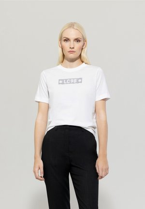 Weißes Baumwoll-T-Shirt mit grafic 'LC98' auf der Vorderseite. Kurzärmlig, runder Ausschnitt, kombiniert mit schwarzen Hosen.