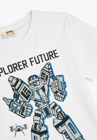 Valkoinen t-paita, jossa on robottigrafiikkaa sinisessä ja mustassa, teksti "TUTKIJA TULEVAISUUS" sekä pieni dronekuva alareunassa.