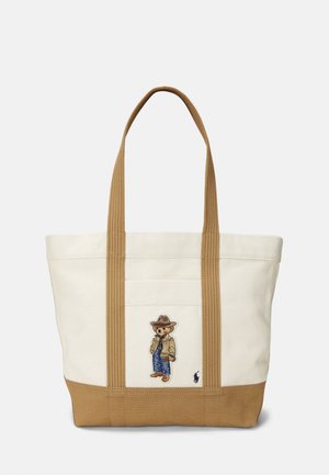 Sac fourre-tout en toile beige et marron avec de longues anses et un ours brodé vêtu d'une tenue de cow-boy sur la poche avant.
