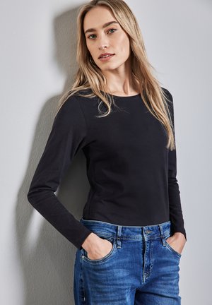 Svart långärmad topp i mjukt tyg, tillsammans med mid-blue denimjeans. Passformen är avslappnad, med rundad halsringning och framfickor.
