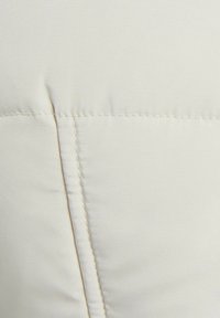 Tessuto color crema con una superficie liscia, caratterizzato da cuciture dettagliate e una cucitura, che indica un design morbido e imbottito.
