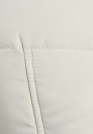 Tela de color crema con una textura suave, que presenta un detallado cosido y una costura, indicando un diseño suave y acolchado.