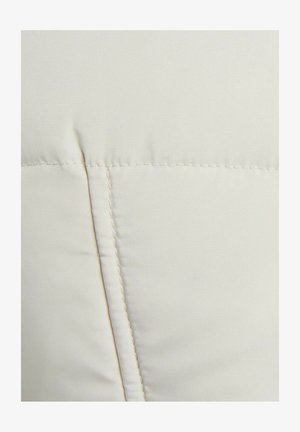 Tela de color crema con una textura suave, que presenta un detallado cosido y una costura, indicando un diseño suave y acolchado.