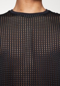 Svart nättröja med vertikala ränder, med en solid svart halsringning och en mjuk textur som avslöjar huden under det öppna väven.