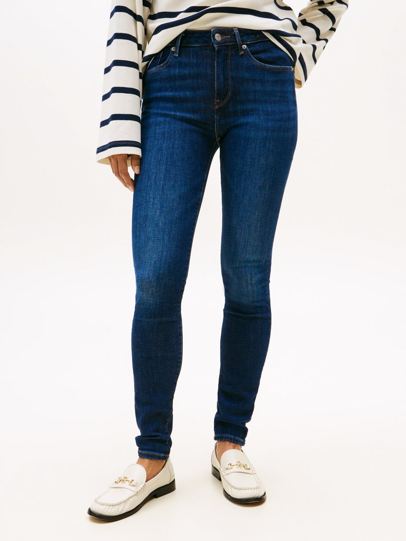 Jean skinny bleu foncé présentant un design classique à cinq poches et des détails de couture subtils, associés à une chemise à rayures à manches longues et des mocassins.