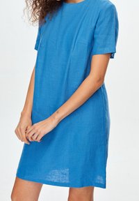 Vestido de lino azul de manga corta con un corte relajado, escote redondo y dos bolsillos frontales. Textura suave y aspecto ligero.