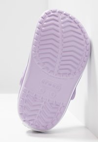 Lila gummiskosula med ett strukturerat greppmönster. Har cirkulära logotyper och en ren design, kantad i vitt för kontrast.