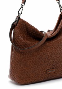 Brązowa, pleciona torba wykonana z teksturowanej skóry. Posiada zakrzywiony kształt oraz odpinany pasek z metalowymi elementami. Zauważalny akcent w postaci logo.
