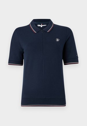 Polo blu navy con colletto con zip, maniche corte e dettagli a righe contrastanti in rosso e bianco sul colletto e sulle maniche.