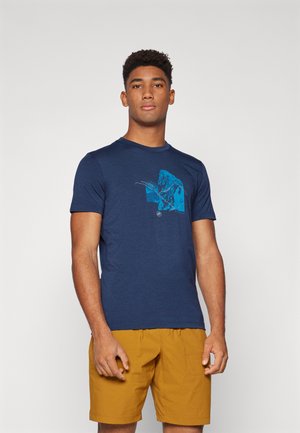 Navy blue t-shirt made of cotton, featuring a graphic design in light blue. Model wears it with mustard yellow shorts.