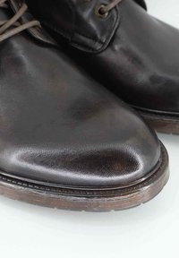 Scarpe in pelle marrone con una finitura lucida, punta arrotondata e suola piatta in gomma. Presentano una semplice allacciatura e dettagli di cucitura lungo il bordo.