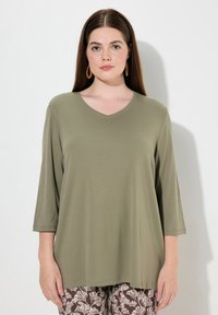 Olijfgroene V-hals shirt met driekwart mouwen, gemaakt van zachte stof, met een losse, relaxte pasvorm en een minimalistisch ontwerp.