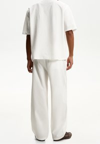 Vit texturerad kortärmad topp och vida byxor, med ett subtilt ribbat mönster. Avslappnad passform med en ren silhuett och neutral färg.