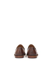 Mocasines de cuero marrón con acabado suave, puntera redondeada y suela de goma plana. La vista trasera muestra un simple detalle de costura y un diseño sin cordones.