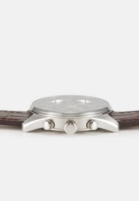 Montre en acier inoxydable avec un cadran rond, bracelet en cuir texturé marron et accents argentés ; présente trois poussoirs de chronographe.