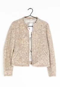 Beige jakke lavet af struktureret stof, med rund halsudskæring, sidelommer foran og en cropped pasform med synlige stikninger.