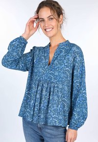 Blaue Bluse mit floralem Muster, tiefem V-Ausschnitt, gepufften langen Ärmeln, gerafftem Taillenbereich und lockerem Schnitt. Sie weist einen komplexen botanischen Druck in Grün und Hellblau auf.