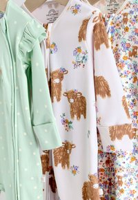 Három baba rugdalózó lóg; egy menta zöld fehér pöttyökkel, egy fehér barna borjúval és virágokkal, egy virágos kis barna borjúkkal.