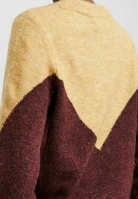 Maglione con design a blocchi di colore, metà superiore gialla e metà inferiore marrone. Finitura in maglia testurizzata con scollo rotondo.