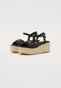 Schwarze Stoff-Espadrille-Plateausandalen mit zwei Knöchelriemen, gewebter Jute-Mittelsohle und dekorativen Schnallen an der Vorderseite.