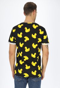 Schwarzes Baumwoll-T-Shirt mit einem Allover-Print von gelben Gummienten mit roten Schnäbeln. Kurze Ärmel mit grauen Akzenten.