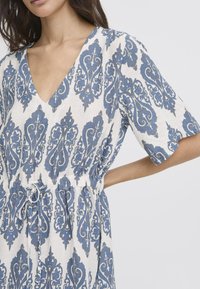 Linnen jurk met bloemenpatroon, voorzien van een diepe V-hals, korte mouwen en een getailleerde taille met een trekkoord. Kleuren: blauw en wit.