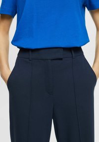 Niebieska bawełniana koszulka zestawiona z szerokimi granatowymi spodniami na wysokim stanie. Spodnie mają gładką fakturę, kieszenie boczne i dopasowany krój.