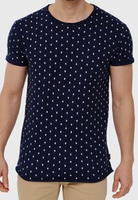 Camiseta azul marino hecha de tela suave, con un patrón de diamantes blancos repetitivo, mangas cortas y cuello redondo.