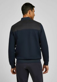 Marineblaue Sweatshirt mit einem kontrastierenden schwarzen Einsatz im oberen Rückenbereich. Eigenschaften: gerippter Saum und Ärmelbündchen, hergestellt aus weichem, strukturiertem Stoff.