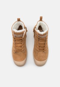 Botine din suede bej cu blană sintetică la interior, talpă din cauciuc și șireturi. Au un guler căptușit și un logo pe limbă.