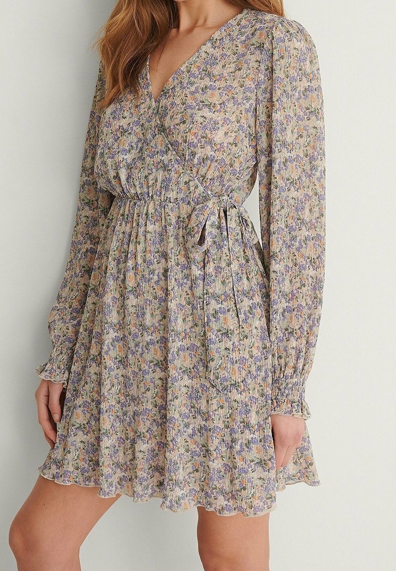 Robe portefeuille florale en tissu léger et texturé. Dotée de manches longues, d'une taille cintrée et d'une jupe évasée avec un ourlet en volants. Les couleurs incluent le violet et l'orange.