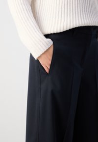 Světlý krémový svetr s ribbed vzorem a volným střihem, doplněný o tmavé elegantní kalhoty s bočními kapsami a hladkým povrchem.