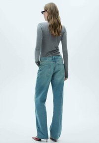 Svetlomodré nohavice s voľným strihom a vysokým pásom, s viditeľným prešívaním a dizajnom piatich vreciek, v kombinácii s priliehavým šedým topom s dlhými rukávmi.